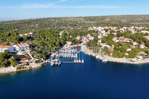 A building land for sale on Brac, Croatia, in coastal area with trees, houses, the sea, and a marina.