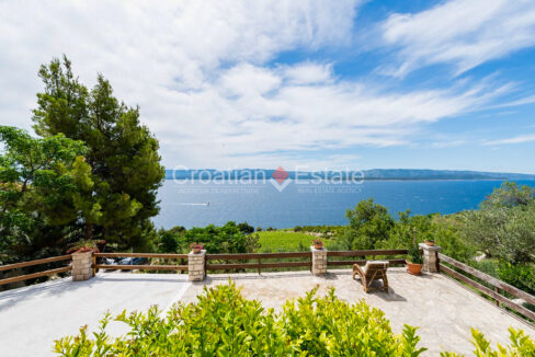 A terrace with plants, an armchair, and a view of the sea and vegetation.