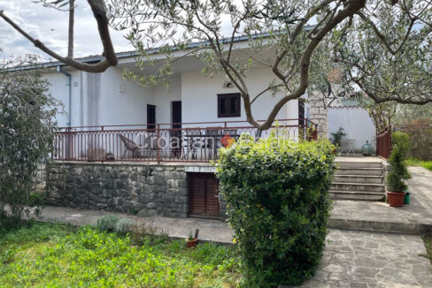 A house for sale on Brac, Croatia, with a partially stone facade, a terrace, and a yard with paved areas and plants.