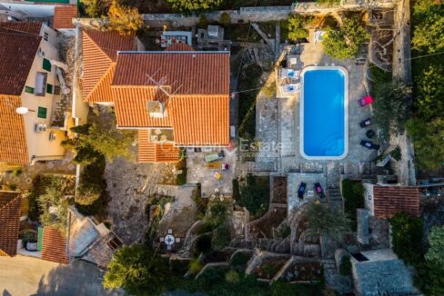 A house for sale on Brac, Croatia, from above, with a patio with a pool, stone tiles, and garden sections with plants.