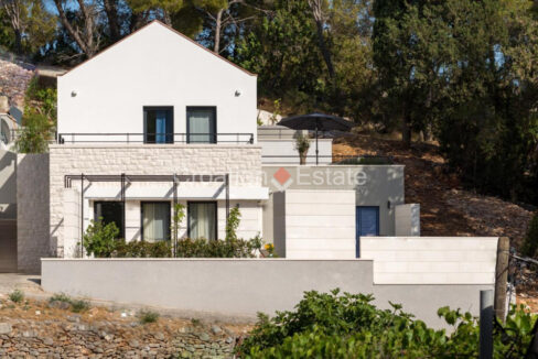 A villa for sale on Brac, Croatia, with terraces, a partially stone facade, and nature behind it.