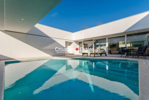 A villa for sale on Brac, Croatia, with a glass wall, and a terrace with a partially covered pool.