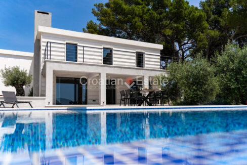 A villa for sale on Brac, Croatia, with a balcony and a terrace with a covered area, a pool, outdoor furniture, and plants.