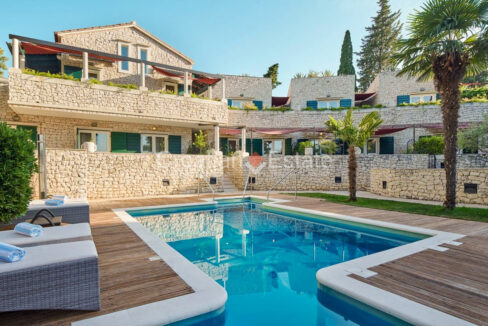A stone villa for sale on Brac, Croatia, with terraces, balconies, and a patio with a pool, a sun deck, and plants.