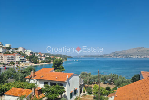 An apartment house for sale on Ciovo, Croatia, with a view of a town, trees, the sea, and a coast with hills.