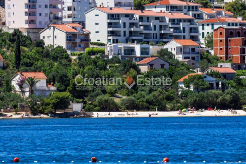 A house with five apartments for sale on Ciovo, Croatia, surrounded by houses and vegetation, and close to a beach.