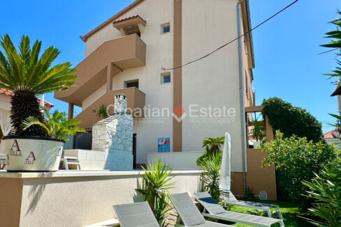 A house for sale on Ciovo, Croatia, with staircases and a courtyard with a stone barbecue, plants, a fence, and sun loungers.