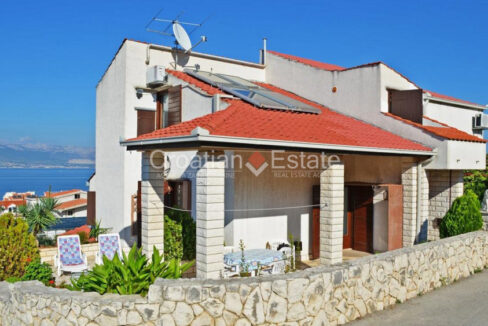 A house for sale on Ciovo, Croatia, with a stone fence and a covered terrace with a table with chairs, and plants.