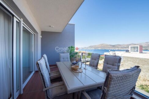 A penthouse for sale on Ciovo, Croatia, with a balcony with an outdoor dining table with chairs and a sea view.