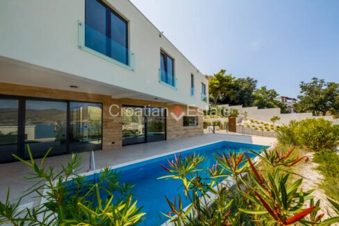 A villa for sale on Ciovo, Croatia, with glass walls and a patio with a pool and plants.