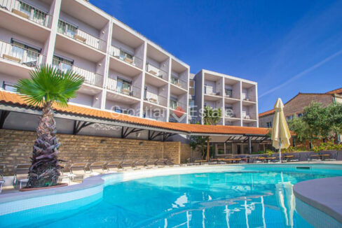 A hotel for sale on Korcula, Croatia, with balconies, a pool, sun loungers, and tables with chairs.