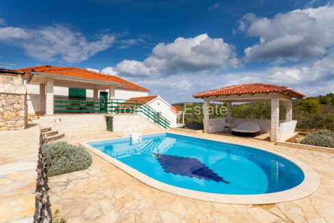 A house for sale on Korcula, Croatia, with a terrace with a pool, canopies, stone tiles, and plants.