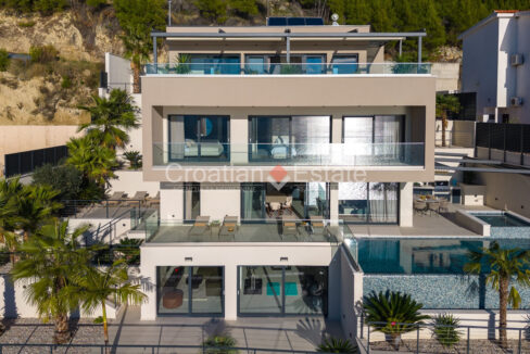 A modern villa for sale in Omis, Croatia, with a terrace with a pool, a balcony, a terrace on the top floor, and plants.