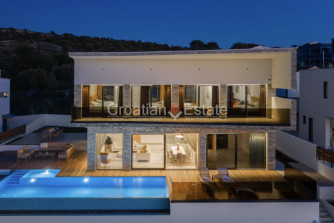 A villa for sale in Rogoznica, Croatia, with glass walls, a balcony, and a terrace with a pool and outdoor furniture.