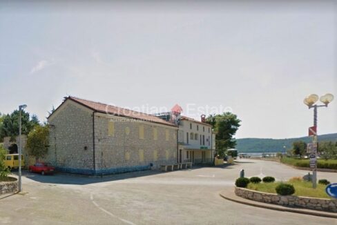 A seafront property for sale in Sibenik, Croatia, with a partially stone facade, pale yellow shutters, and a road next to it.
