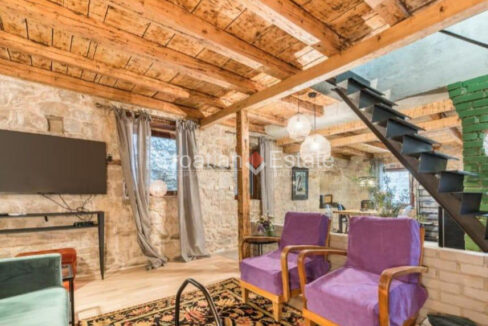 A stone house for sale in Grad, Split, Croatia, with a living room with a TV set, furniture, a wooden ceiling, and stairs.