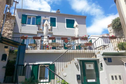 A house for sale in Split, Croatia with green shutters, stairs and a spacious terrace in front with tables, chairs and sun umbrellas.