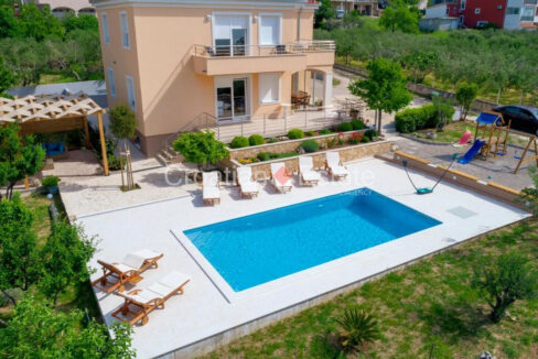 A house for sale near Split, Croatia, with balconies, a terrace, and a patio with a pool, plants and a children's playground.