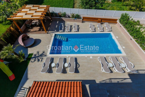 A villa for sale near Split, Croatia, with a patio with a pool with stairs, outdoor furniture, a canopy, plants, and a fence.