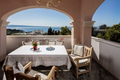 An apartment for sale in Split, Croatia, with a loggia with a dining table, benches, a chair, arches, and a sea view.