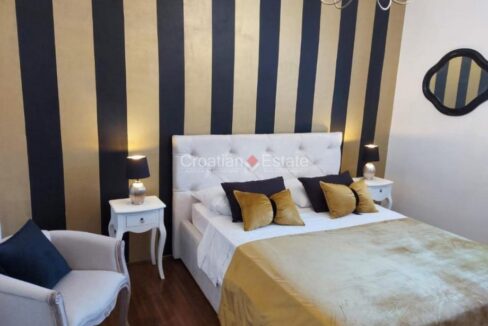 An apartment for sale in Radunica, Split, Croatia, with a bedroom with a double bed with nightstands and a decorative wall.