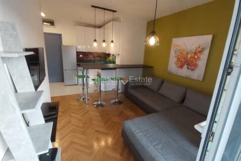 An apartment for sale in Split, Croatia, with an open-concept living room with a sofa and a TV set, a dining area with a bar table and chairs, and a kitchen.