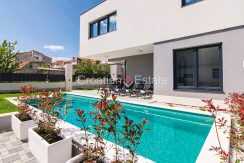 A villa in a complex of two villas for sale near Split, Croatia, with a patio with a pool, plants, and a covered area.