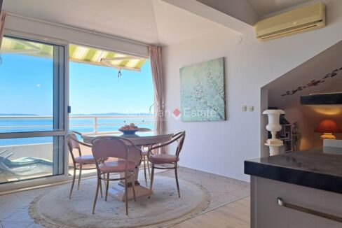 An apartment for sale in Split, Croatia, with a dining area, and a large glass, sliding door of a loggia with a sea view.