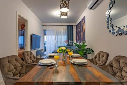 A flat for sale in Znjan, Split, Croatia, with an open-plan dining room with a table with armchairs and a living area behind.