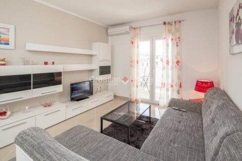 An apartment for sale in Strozanac, Croatia, with a living room with furniture, a TV set, an air conditioner, and glass doors to a loggia.
