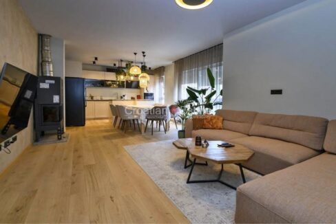 A flat for sale in Strozanac, Croatia, with an open-plan living room with a fireplace, a dining area, and a kitchen.