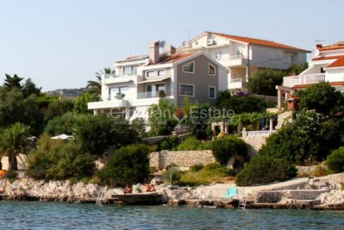 A seafront villa for sale in the Trogir area, Croatia, with a terrace, balconies, and houses and vegetation around it.