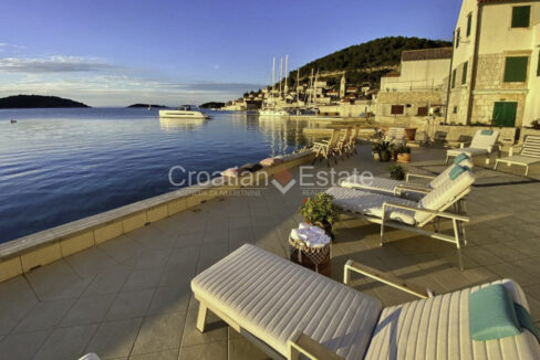 A seafront villa for sale on Vis, Croatia, with a seafront terrace with a view of the sea, boats, houses, and vegetation.