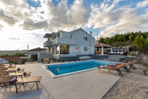 A villa for sale in Zrnovnica, Split, Croatia, with balconies, terraces, stairs, a pool, sun loungers, and a fence.