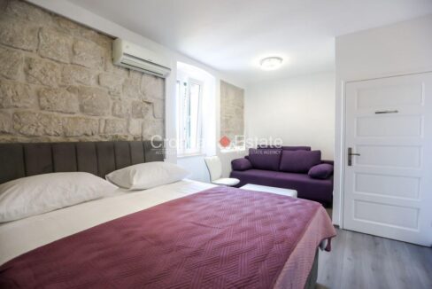 A house for sale in Split, Croatia, with a bedroom with a double bed, a stone wall, an air conditioner, a window, and a sofa.