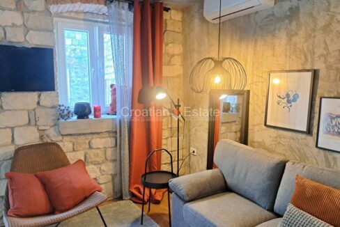 A stone house for sale in Kastel Luksic, Croatia, with a living room with a stone wall, an air conditioner, and a sofa.