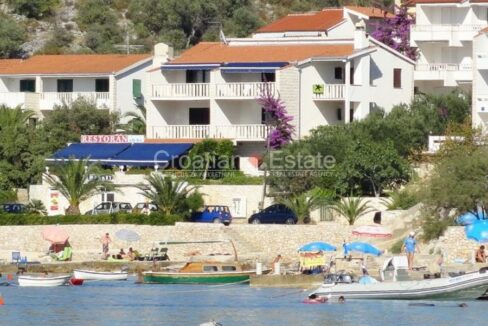 A seafront hotel for sale in Rogoznica, Croatia, with balconies and a restaurant terrace, a beach, and the sea with boats.